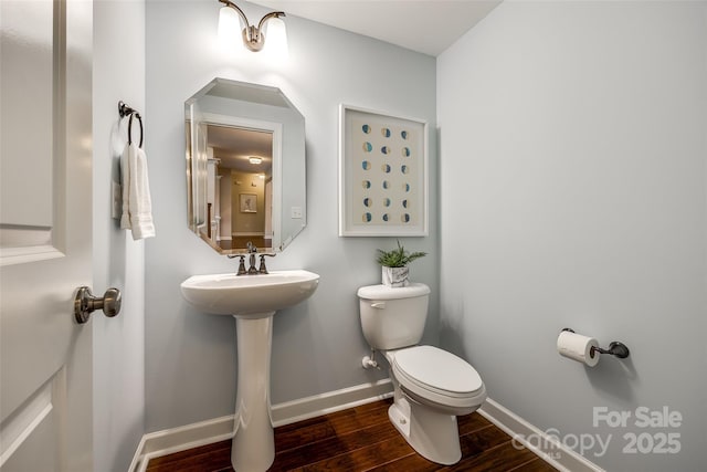 half bathroom with toilet, wood finished floors, baseboards, and a sink