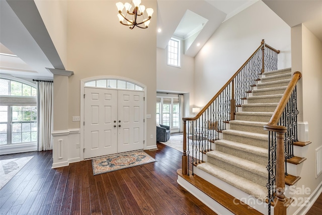 foyer entrance featuring stairway, hardwood / wood-style flooring, a chandelier, a high ceiling, and a wainscoted wall