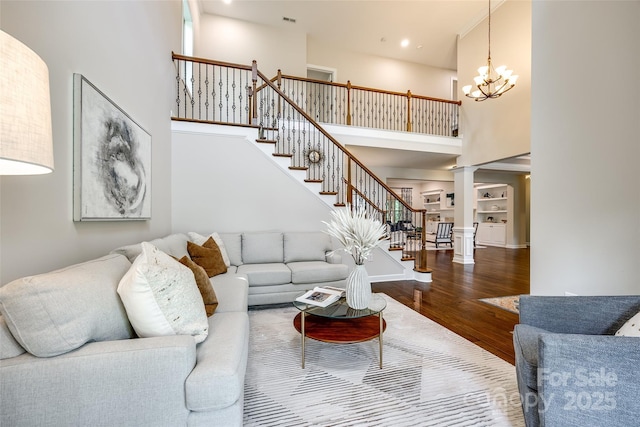 living area featuring wood finished floors, stairway, a towering ceiling, a chandelier, and ornate columns