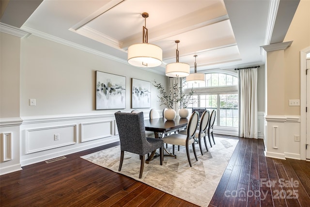 dining space with hardwood / wood-style floors, a raised ceiling, crown molding, wainscoting, and ornate columns