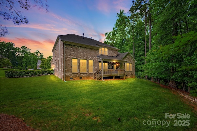 rear view of property featuring crawl space, brick siding, a lawn, and a wooden deck