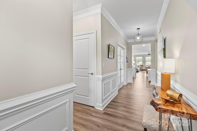 corridor with crown molding, wainscoting, light wood-style flooring, and a decorative wall