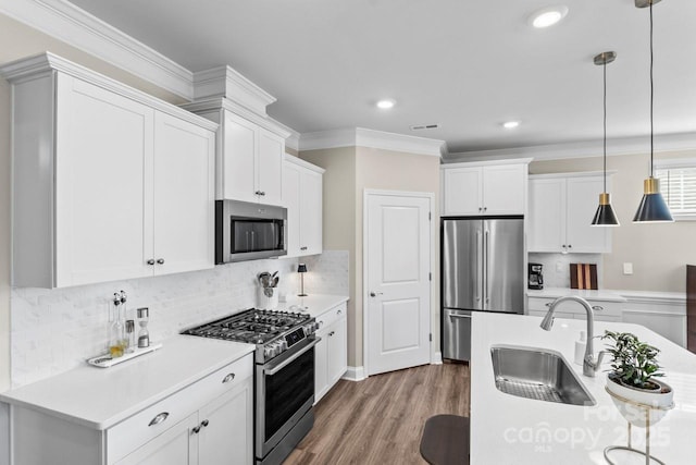 kitchen featuring pendant lighting, a sink, light countertops, ornamental molding, and stainless steel appliances