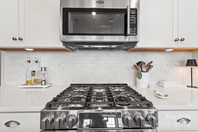 kitchen with appliances with stainless steel finishes, tasteful backsplash, light stone countertops, and white cabinetry
