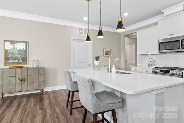 kitchen with backsplash, appliances with stainless steel finishes, dark wood finished floors, a sink, and an island with sink