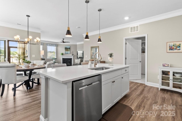 kitchen with crown molding, wood finished floors, dishwasher, a sink, and a glass covered fireplace
