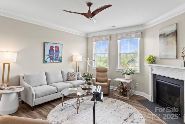 living area featuring ceiling fan, crown molding, wood finished floors, baseboards, and a glass covered fireplace