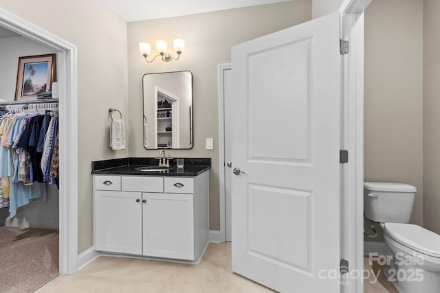 bathroom with toilet, baseboards, a walk in closet, and vanity