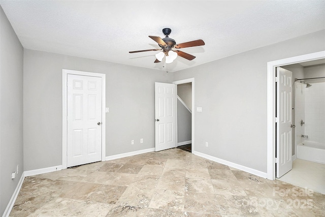 unfurnished bedroom with baseboards, ensuite bathroom, ceiling fan, stone finish floor, and a textured ceiling