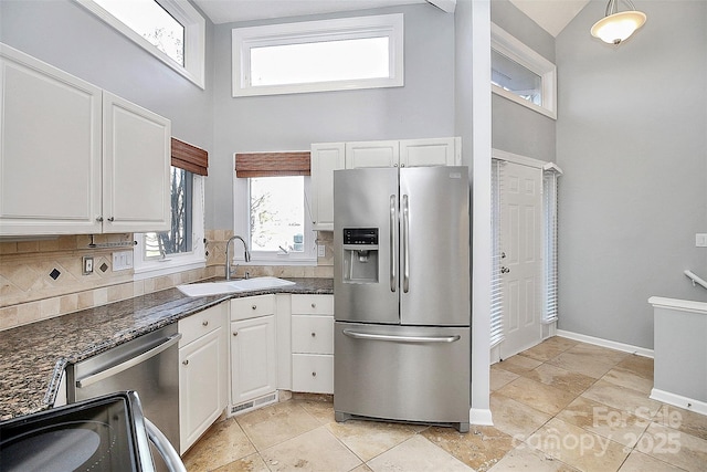 kitchen with a high ceiling, a sink, stainless steel appliances, white cabinetry, and backsplash