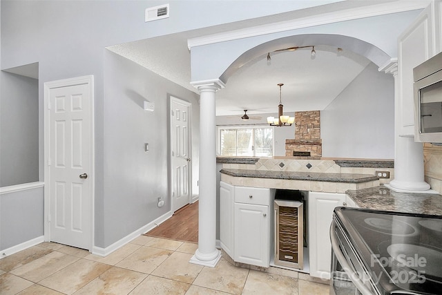 kitchen featuring arched walkways, white cabinetry, decorative backsplash, ornate columns, and visible vents