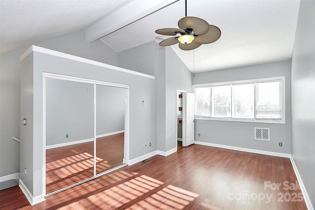 unfurnished bedroom featuring baseboards, wood finished floors, beamed ceiling, visible vents, and a closet