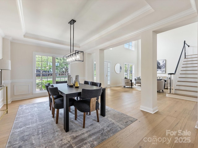 dining space featuring crown molding, light wood finished floors, a tray ceiling, and stairway