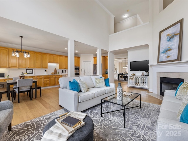 living room with crown molding, a towering ceiling, light wood finished floors, and a tile fireplace