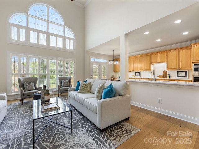 living room with an inviting chandelier, ornamental molding, wood finished floors, baseboards, and recessed lighting