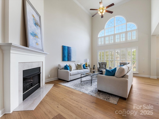 living area with ceiling fan, baseboards, wood finished floors, a high end fireplace, and ornamental molding