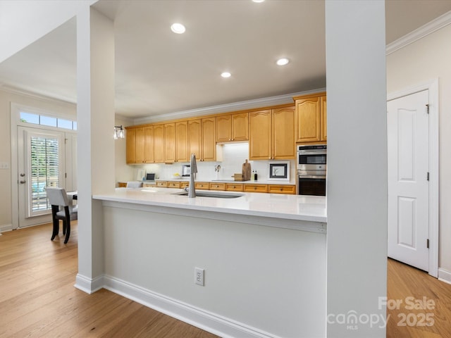 kitchen featuring stainless steel double oven, a sink, baseboards, light wood-type flooring, and ornamental molding
