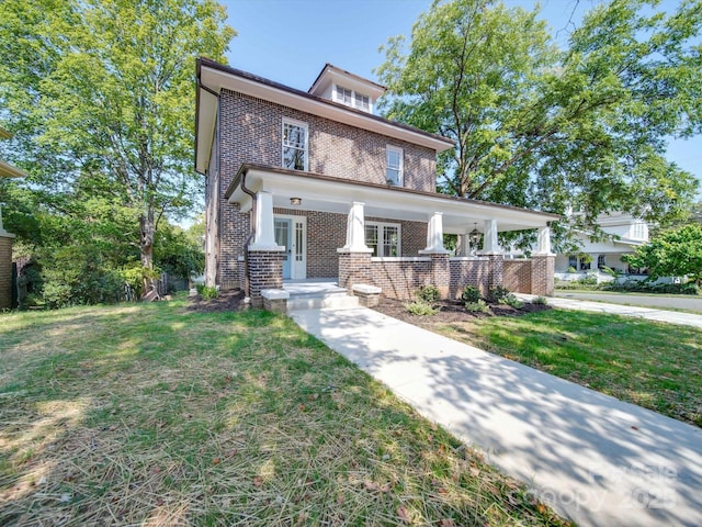 american foursquare style home featuring covered porch, brick siding, french doors, and a front yard