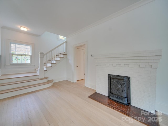 unfurnished living room featuring stairway, crown molding, a brick fireplace, and wood finished floors