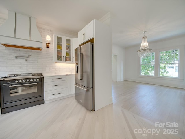 kitchen with high end fridge, light wood-style floors, range with two ovens, tasteful backsplash, and custom exhaust hood