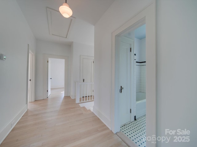corridor with baseboards, an upstairs landing, attic access, and light wood-style floors