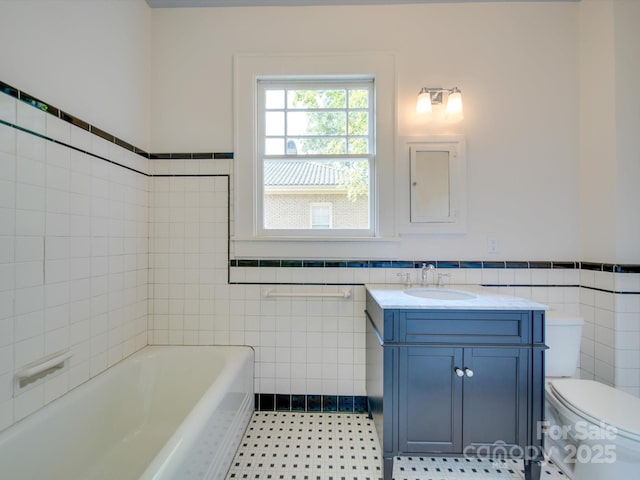 bathroom with vanity, wainscoting, toilet, tile walls, and a tub to relax in