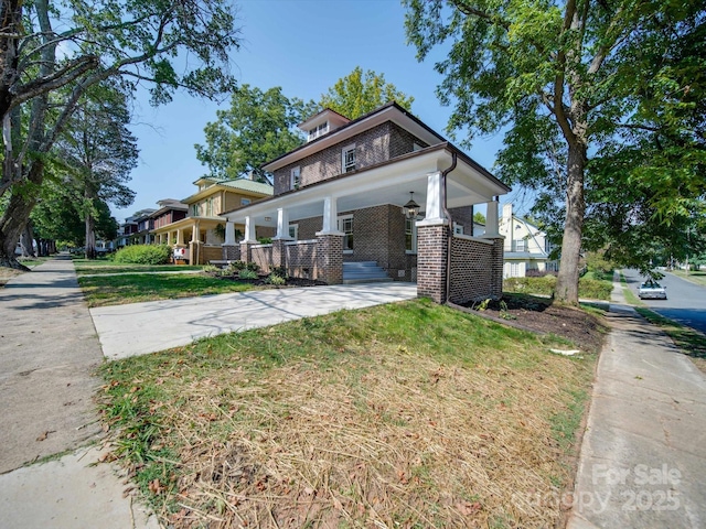 view of front of home featuring a porch, driveway, a carport, brick siding, and a front lawn