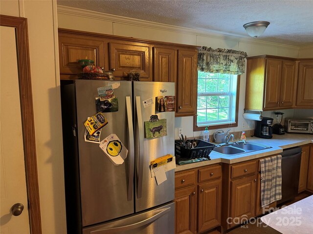 kitchen with a sink, a textured ceiling, freestanding refrigerator, and brown cabinetry