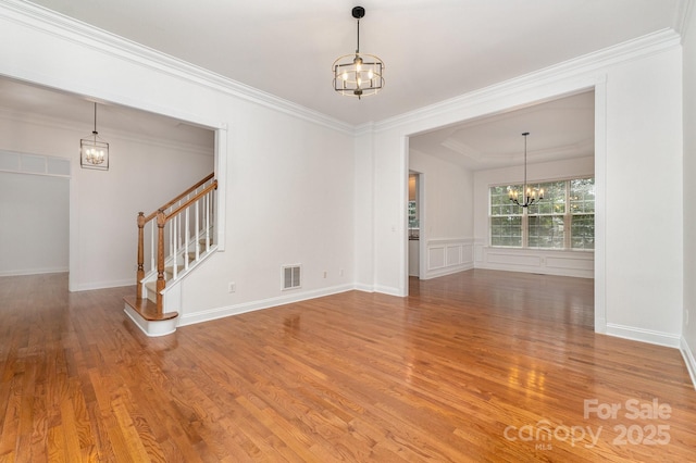 empty room with visible vents, ornamental molding, wood finished floors, and a notable chandelier