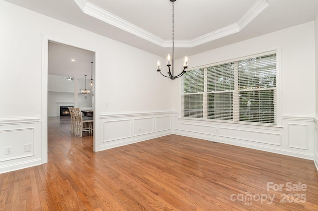 unfurnished dining area featuring an inviting chandelier, a raised ceiling, and crown molding
