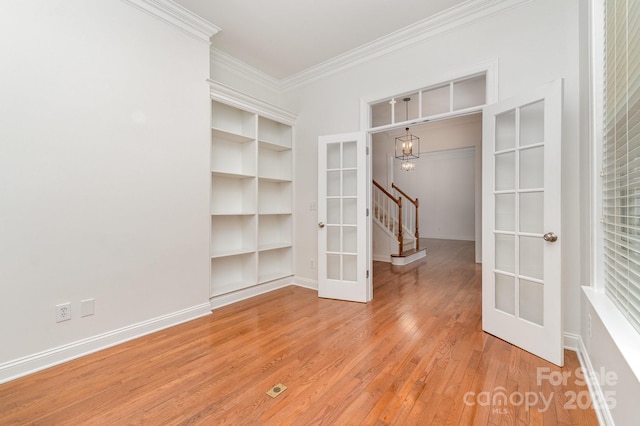 unfurnished room with french doors, crown molding, a notable chandelier, light wood-style floors, and stairs