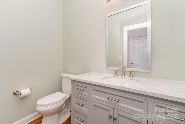 half bath with toilet, baseboards, wood finished floors, and vanity