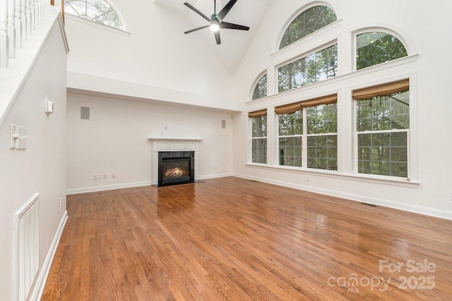 unfurnished living room with ceiling fan, visible vents, a fireplace with flush hearth, wood finished floors, and high vaulted ceiling