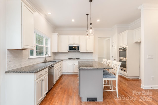 kitchen featuring a sink, dark stone countertops, stainless steel appliances, white cabinetry, and a kitchen bar