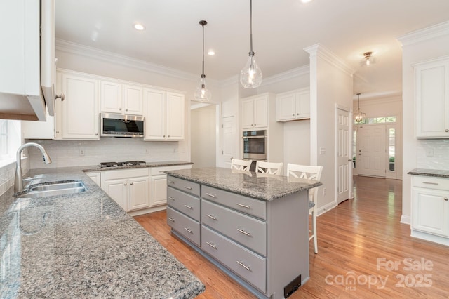 kitchen featuring a kitchen island, a breakfast bar area, gray cabinets, a sink, and appliances with stainless steel finishes