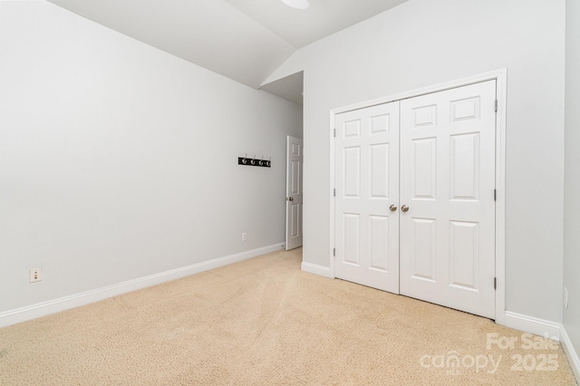 unfurnished bedroom featuring baseboards, light colored carpet, vaulted ceiling, and a closet