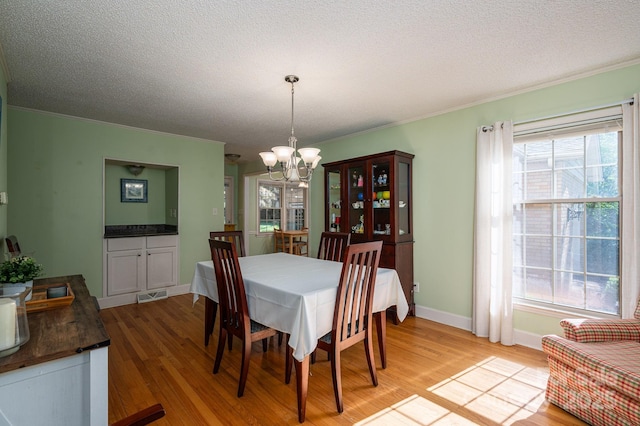 dining room with a chandelier, light wood-style floors, crown molding, baseboards, and a textured ceiling