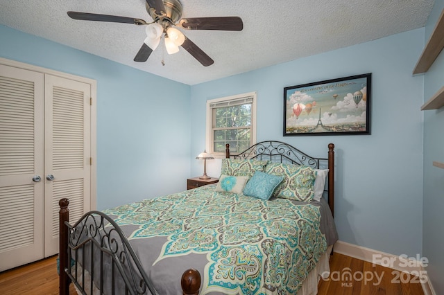 bedroom featuring a closet, wood finished floors, a textured ceiling, baseboards, and a ceiling fan