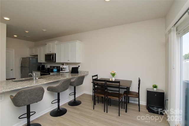 kitchen with light wood-type flooring, a sink, white cabinets, stainless steel appliances, and recessed lighting