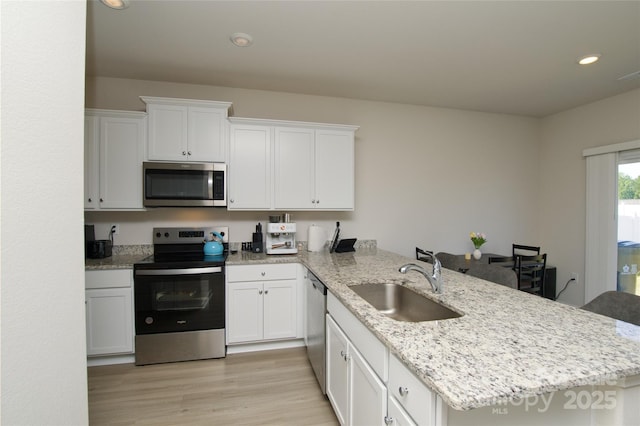 kitchen with white cabinetry, a sink, a peninsula, stainless steel appliances, and light wood-style flooring