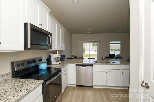 kitchen with a sink, light stone counters, light wood finished floors, stainless steel appliances, and white cabinetry