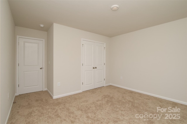 unfurnished bedroom with baseboards, a closet, and light colored carpet