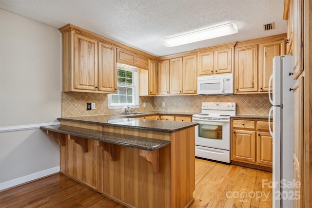 2196 Uphill Ln, Lenoir, NC 28645 - kitchen featuring white appliances, a peninsula, light wood-style floors, a kitchen breakfast bar, and a textured ceiling