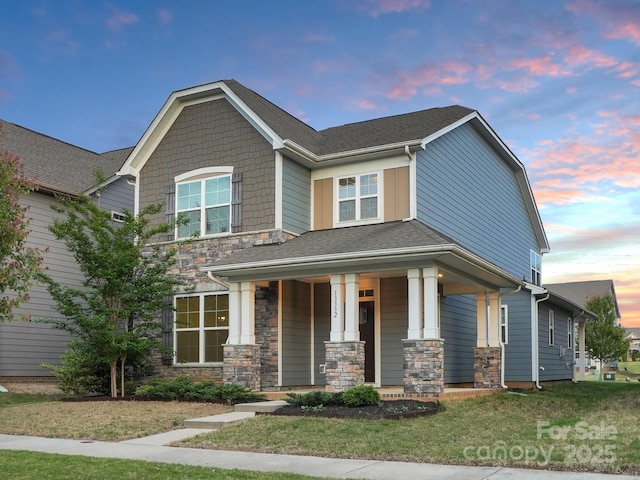 craftsman inspired home featuring a front yard, roof with shingles, covered porch, and stone siding