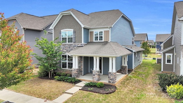 craftsman-style home featuring roof with shingles, a front lawn, stone siding, a porch, and cooling unit