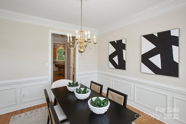 dining area featuring an inviting chandelier, a decorative wall, a wainscoted wall, wood finished floors, and ornamental molding