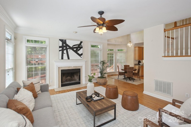 living room featuring visible vents, crown molding, wood finished floors, a fireplace, and a ceiling fan