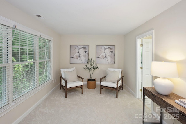 living area featuring baseboards, visible vents, and light colored carpet