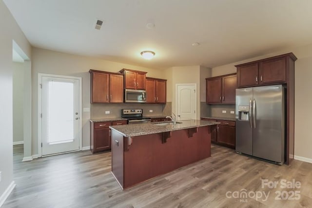 kitchen featuring appliances with stainless steel finishes, a sink, wood finished floors, a kitchen bar, and baseboards