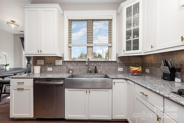kitchen with stainless steel dishwasher, backsplash, a sink, and white cabinets